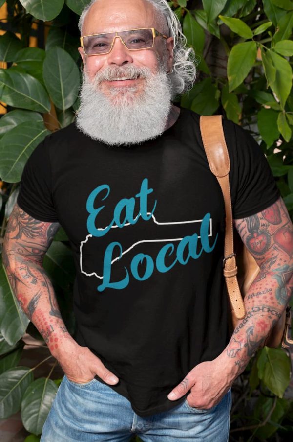 Older Hipster wearing glasses, shirt says Eat Local